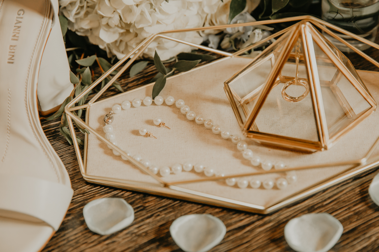 This Image is of a wedding flat lay that features a wedding ring, pearl necklace and pearl earrings.