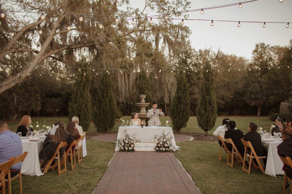 Person giving heartfelt wedding speech with happy couple in background